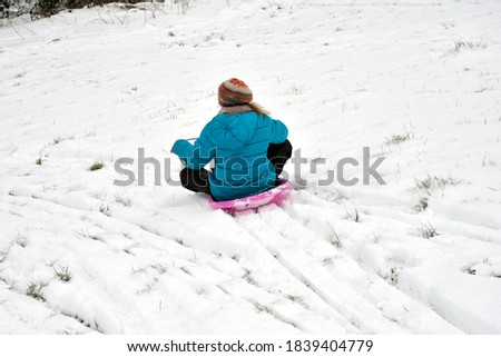 winter snow scene with young girl sledging down snowy bank in a bright blue coat and pretty colored hat.  one person tobogganing fun  in wintertime