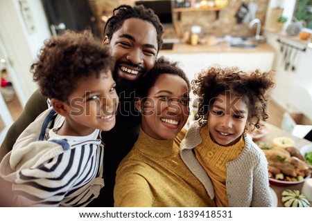 Happy black family having fun on Thanksgiving while taking selfie in dining room. 