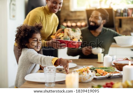 Happy African American family serving food for Thanksgiving lunch at dining table. Focus is on little girl. 