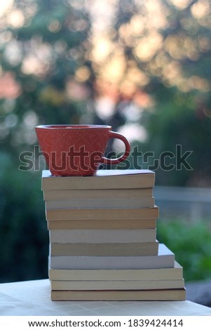 Stack of paperback books and cup of tea or coffe in teh garden. Selective focus.