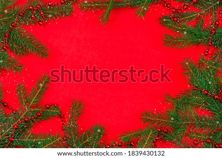 Christmas tree branches with red beads, snow, snowflakes with copy space in the center on a red background, top view. Greeting card for Christmas and new year. Beautiful Christmas background.