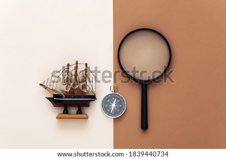 Minimalism travel, adventure flat lay. Compass, ship and magnifier on brown beige background. Top view