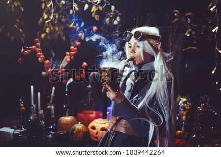 Halloween elf with magic magic in the dark forest. Beautiful young woman in a hat and elf costume holding magical chemistry. Halloween art design