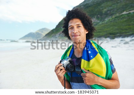 Brasil soccer fan tourist with camera and flag smiling happy at the beach
