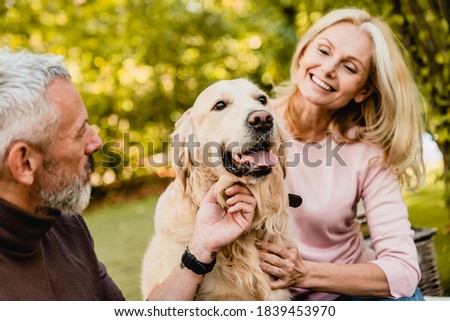 Happy caucasian senior couple petting their dog in autumn park Royalty-Free Stock Photo #1839453970