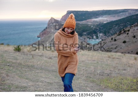 Hipster woman traveler wearing knitted sweater and hat walking  on top of the mountain landscape and looking to the sea