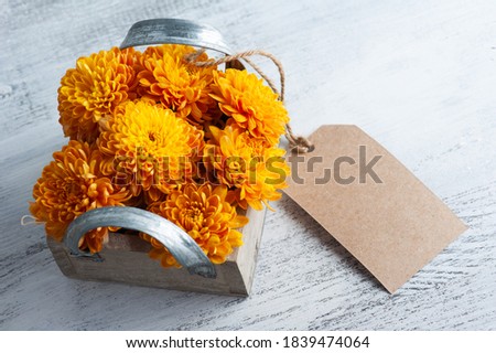 Orange chrysanthemum flowers in wooden box on rustic background. Greeting card with tag and copy space for your text