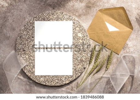 Autumn stationery composition. Blank white memo cards mockup on granite plate, craft envelope, ears of wheat and silk ribbon. Beige grunge background. Top view, flat lay