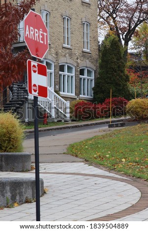 stop sign, translation of (Stop) in English, with a sidewalk, trees, green grass, an old brick building and stairs
