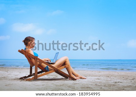 woman in bikini sitting with laptop on the beach