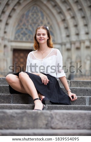 Young positive female sitting on stone stairs at the street