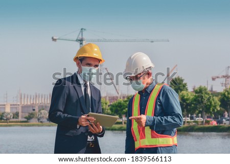 Two people workman worker working on site construction And then talking discussion building project by tablet And using face mask protect coronavirus covid 19