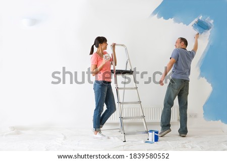 Woman leaning on ladder and watching man paint wall with paint roller