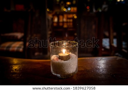 Isolated tealight inside a glass illuminating a dark scene and reflections on a wooden table and a nice bokeh background