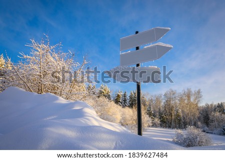 Blank signpost with three white arrows against beautiful blue sky in sunny frozen day. Blank track pointers or guide post on winter background with copy space. Icicles on signpost in sunlight.