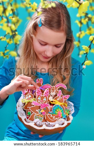 beautiful young girl holding a basket with homemade easter gingerbread cookies on blue background