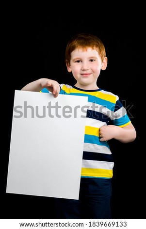 a beautiful boy holds a large sheet of clean white paper in his hands, a close-up portrait of a cute red-haired child