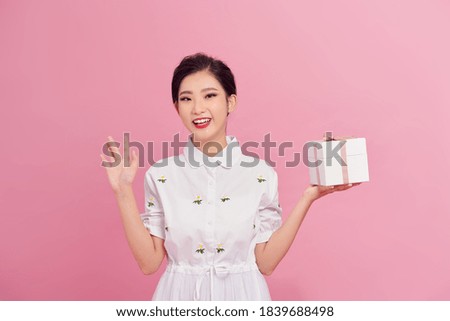 Picture of happy asian girl child standing isolated over pink background. Looking camera holding gift box surprise.