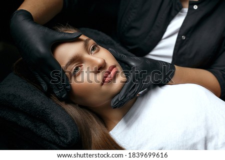 Beauty stylist in a gloves touching lovely woman's face before permanent makeup procedure Royalty-Free Stock Photo #1839699616