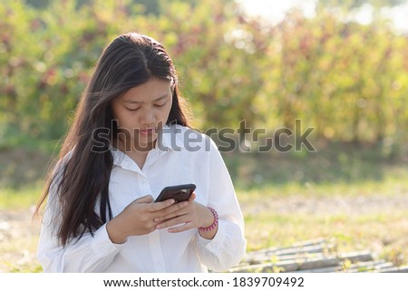 Cute asian girl wearing white shirt is playing smartphone in park.