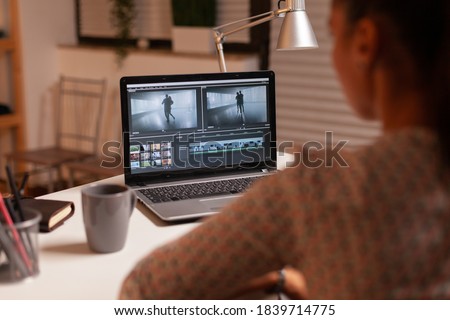 Brunette video editor works with footage on personal laptop in home ktichen during night time. Content creator in home working on montage of film using modern software for editing late at night.