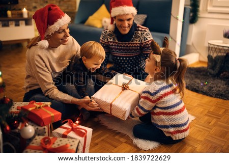 Happy parents and their kids having fun while opening gifts on Christmas eve at home.