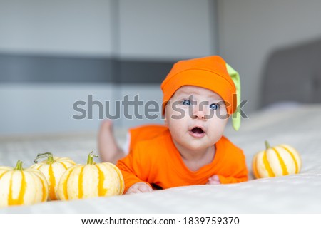 High Angle View Of Baby In Pumpkin Costume. Happy Kid two months old in orange Halloween costume on bed
