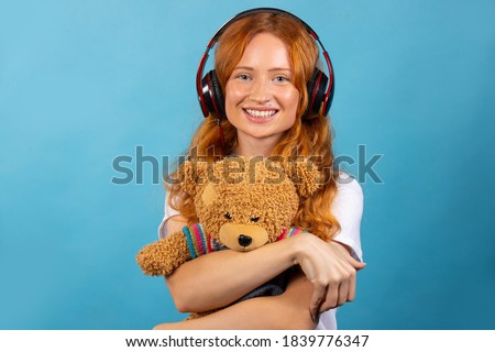 Girl with her beloved bear. Listens to music with headphones, posing and smiling. Photo on a blue background