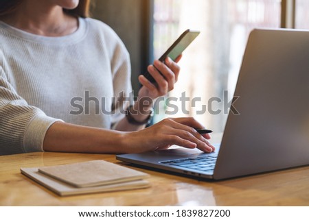 Closeup image of a woman holding and using mobile phone and laptop computer in office