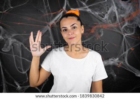 Young beautiful woman over black background with cobwebs and spiders doing hand symbol