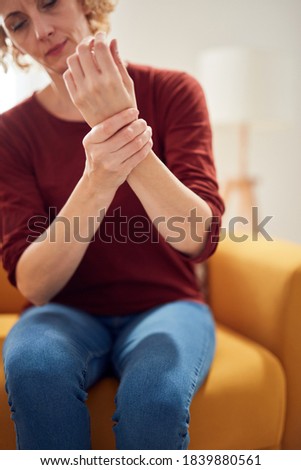 Woman with hand pain sitting on a couch at home.