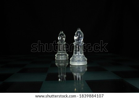 two clear chess piece bishop isolated on a chequered chess board with a black background