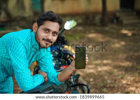 Young Indian boy in ethnic wear and showing smartphone with new bike