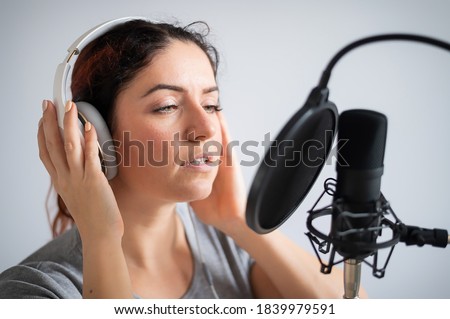 A woman with headphones is recording a song in a recording studio. Emotional girl sings with pleasure