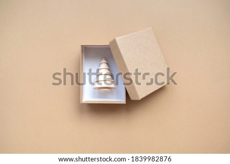 Small gift box with a wooden Christmas tree for decoration inside on a beige background. the idea of a Christmas gift. The concept of minimalism
