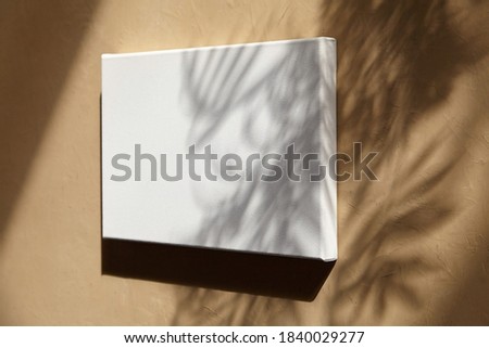 Blank canvas hanging on wall with sunlight and shadow of leaves. Mockup empty quote board, white cotton canvas
