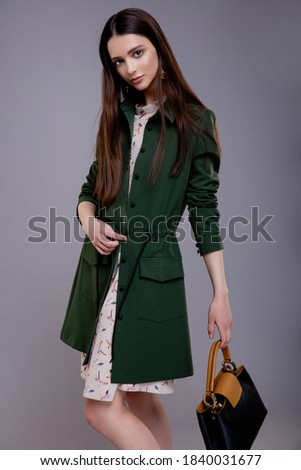 High fashion photo of elegant woman, model in pretty green coat with bag, handbag, beautiful young woman. Studio shot. Fire extinguisher in hands. Gray background. Slim figure. Make up, hairstyle