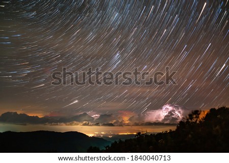 Star trails above storm over the town