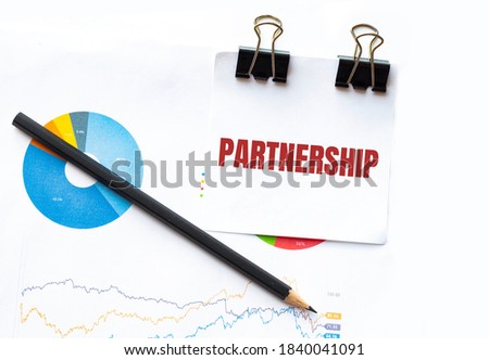 Notepad with text PARTNERSHIP on business charts and pen