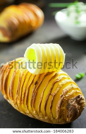 Sliced potato baked in foil and topped with a curl of creamy golden butter to be served as a delicious vegetable accompaniment or appetizer to a meal