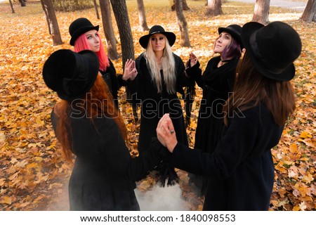 Coven of witches, modern witches gathered and do a ritual in the Park. Halloween, a group of different women like witches in black and hats.
