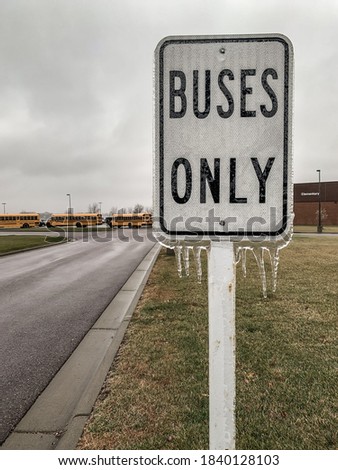 freezing rain causing a buildup of ice on a bus sign outside a school