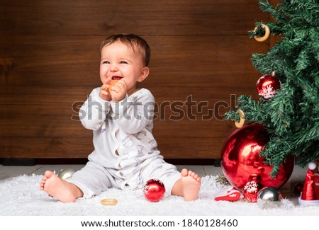 cute baby sits on the floor near the Christmas tree on a wooden background. baby eating a bagel
