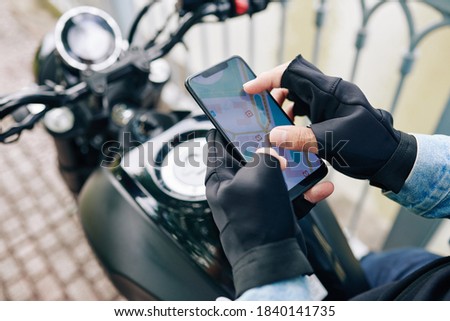 Hands of motorcyclist zooming in map on smartphone screen before riding to destination point