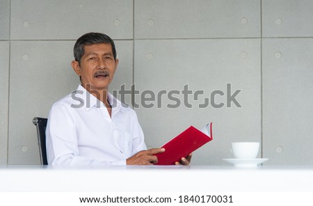 Work from home and social distancing concept. Asian business old man  working at co-working space or meeting room. Aging man read report or book and drinking coffee