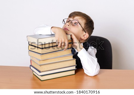 Education concept. The student sits at the table and holds his head, hands operate on the stacked books, looks up. Isolated on white background.