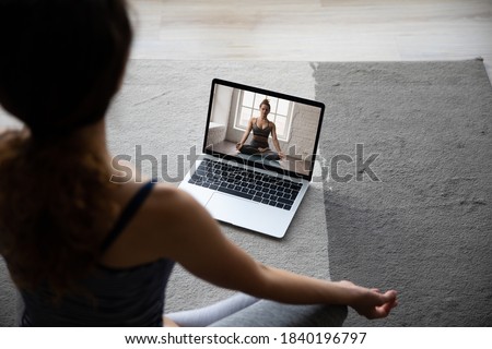 Back view of fit sporty woman sit on floor at home mediate practice yoga having video call with coach. Female do exercises watch stretching class on computer online, take distant course or lesson. Royalty-Free Stock Photo #1840196797