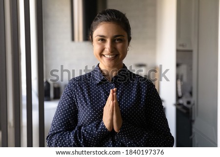 Portrait of smiling young Indian woman look at camera pose hold hands in Namaste gesture. Happy millennial ethnic female feel religious superstitious praying at home. Religion, faith concept.