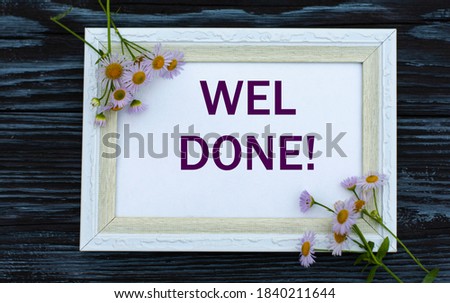 WEL DONE - words in a white beautiful frame on a black wooden background with delicate colors. Business and announcement concept