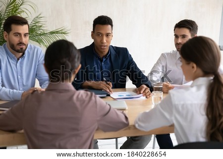 Multiethnic businesspeople talk at business meeting office, discuss cooperation or partnership together. Diverse multiracial partners negotiate brainstorm at briefing at workplace. Teamwork concept.